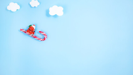 Santa Claus on a sleigh of candy canes flies down from under the clouds. Blue background.