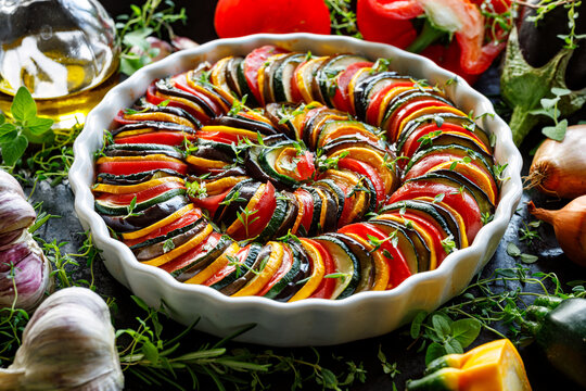 Colorful vegetarian provence casserole, Tian made of vegetable slices in a ceramic casserole dish on a dark background, close up view