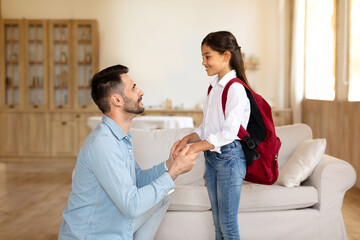 Loving dad preparing schoolgirl daughter with backpack for school indoor