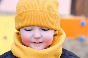 Portrait of a toddler baby boy in a yellow hat and scarf. Kid aged two years (two-year-old boy)