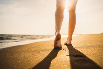 detail of legs walking on the sand of the beach next to the sea shore at sunset