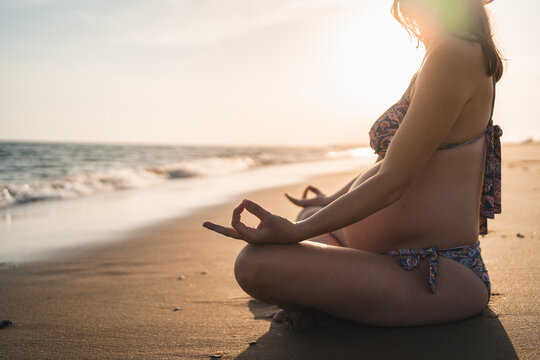 Pregnant Woman Meditating Sitting On The Beach Shore Looking Out To Sea