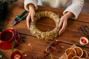 winter holidays, diy and hobby concept - close up of woman with decorations making christmas wreath...
