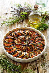 Provence tian,  ratatouille from sliced vegetables in a baking dish on a wooden table, close-up...