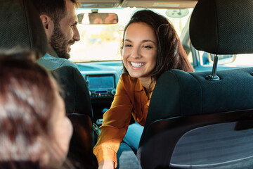 Young european family sitting in new car, mother smiling and talking to her daughter, enjoying road...