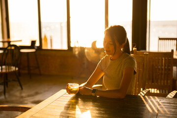 Woman in coffee shop under sunset sunlight flare - obrazy, fototapety, plakaty