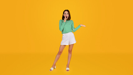 Amazed pretty young woman showing blank space on yellow background