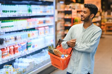 Portrait of handsome young Indian man standing at grocery shop or supermarket, Closeup. Selective Focus.
