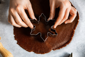 baking, cooking and christmas concept - close up of hands with mold cutting gingerbread dough on black kitchen table top