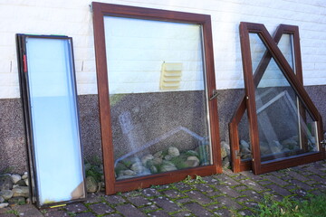 Old wooden windows stacked near the building. Replacement by new plastic windows, building renovation works. Replace old window, installing double glazed PVC. - 651997049