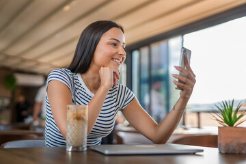 One young woman sitting in cafe working and looking at mobile phone, making a video call or taking photos, modern lifestyle concept