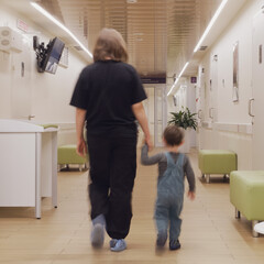 The baby tightly holds onto his mother's arm while they walk through the pediatric hospital ward. Kid aged two years (two-year-old boy)
