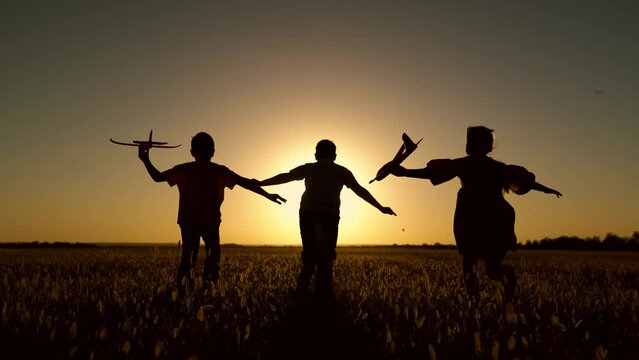 Children play with toy plane. Happy children run with toy plane across field at sunset. Boy, girl wants to become pilot, astronaut. Slow motion. Teenager dreams of flying, becoming pilot. Silhouette