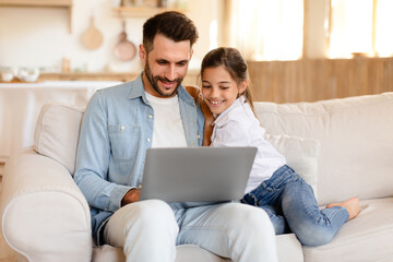 Fototapeta premium Cheerful daddy and daughter having fun with laptop at home