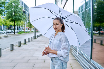 Young teenage female on summer cloudy day under white umbrella on city street