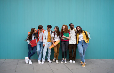 Large group of cheerful young people leaning against blue wall. Multicultural college students...