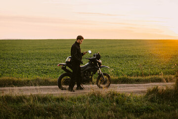 male motorcyclist on a country road with an enduro motorcycle at sunset.