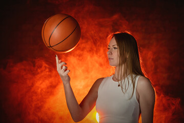 Young girl with the basketball ball posing on the red color smoke background.
