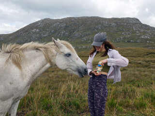 Beautiful nature scenery wit beautiful young woman feeding white horse with mountains in the...