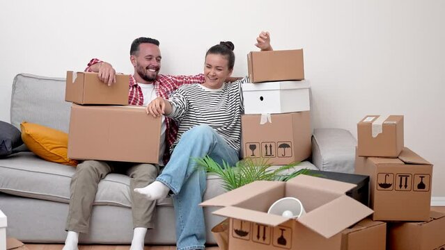 a happy young married couple relaxing on sofa with many cardboard boxes, exhausted but happy after moving to new apartment 