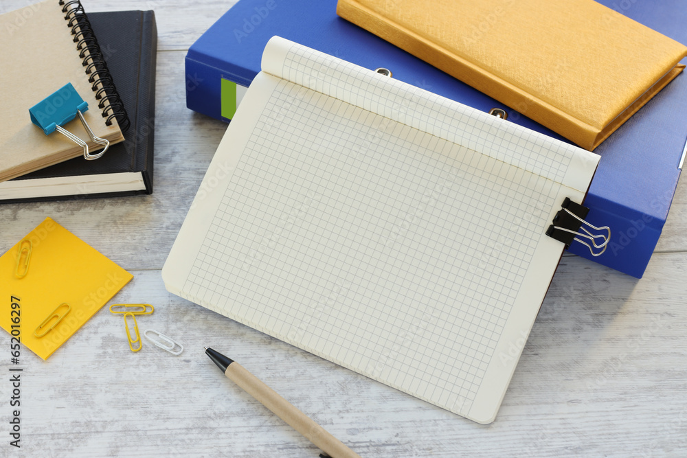 Poster a blank notepad with a pen sits near a blue folder on a wooden table with a yellow notepad and suppl