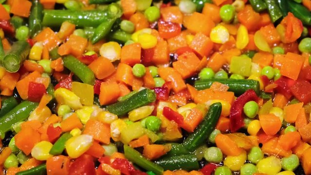 Cooking of frozen traditional mexican vegetable mix. Mixing with a spatula. Frying of carrots, green beans, corns. Melting ice on hot pan. Fast healthy food. Vegan dish. Bright colorful ingredients.