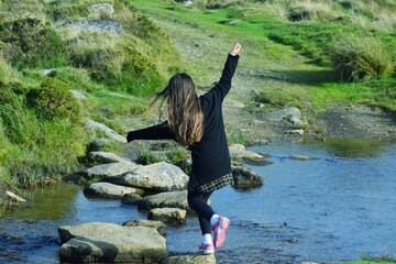 Young girl hopping across a stream on stepping stones. 