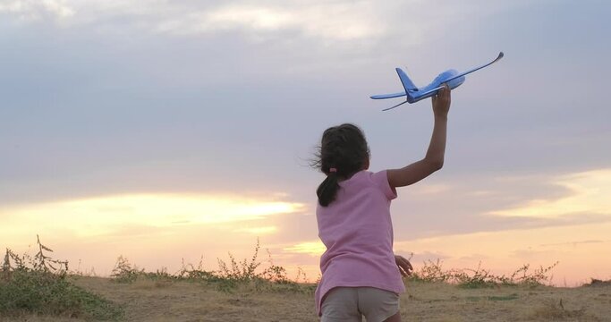 Happy kid girl runs with a toy airplane at sunset. Dream of becoming a pilot. Silhouette of happy kid in nature. Children dream. Silhouette shot