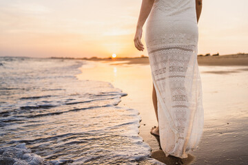 half body of beautiful woman walking along the beach shore with sunset light dressed in white