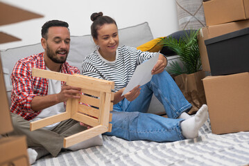 A couple, surrounded by moving boxes, assembles a DIY shelf, customizing their new living space.