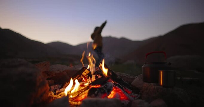Child and campfire flame at dusk. Slow motion. Halt for night in mountains in wild deserted area. Cinematic. Blurred background. The child plays in airplane, runs in circle with his arms outstretched