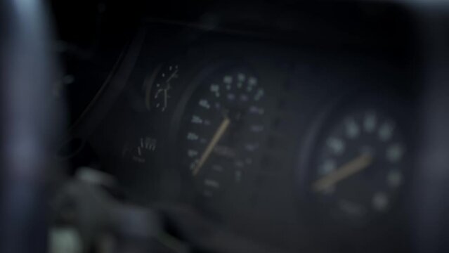 Close view of the dashboard and speedometer of an abandoned and dilapidated 1970s rally car resting in a scrap yard. The car has spider webs and dust on all surfaces. 