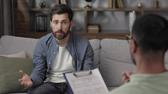 Visit to a psychologist. A man sits on a couch and talks to a psychotherapist. The patient is depressed, apathetic and stressed from problems in his personal life. Help of a psychologist.