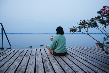 A woman on a pier with a phone takes pictures of birds