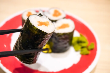 Close up photo of someone eating salmon sushi roll using chopsticks on Japanese Restaurant. Concept for whole healthy food, nutrition, omega-3, animal protein, seafood, modern resto and street food. 