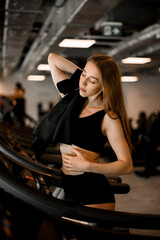 Side view on tired after workout pretty woman making pause and wipes sweat from the body with black towel