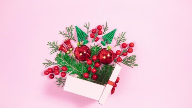 Christmas decorations and small Christmas trees  near the pink gift box. Thuja branches appear and disappear. Pink background. Holiday greeting card. Copy space. Stop motion animation.
