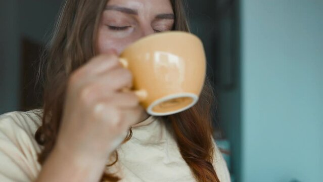 Close up of attractive peaceful dreamy woman holding cup enjoy tea or coffee drink morning invigorating coffee beverage while sits on her terrace. 