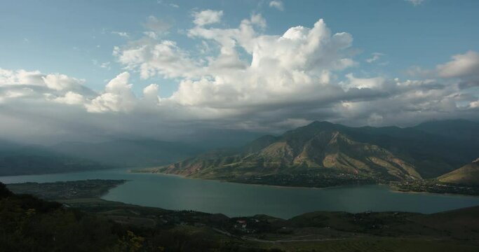 Mountain landscape timelapse video for background. Clouds over a lake or reservoir in the Charvak mountains, in the pre-sunset rays of the sun. Foggy haze, the rays of the sun penetrate the landscape
