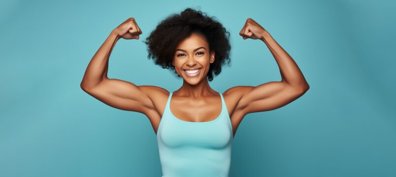 attractive young african american woman flexing her biceps on teal background