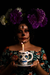 Joven mujer con maquillaje de catrina y semblante tenebroso sostiene vela en una taza de calavera