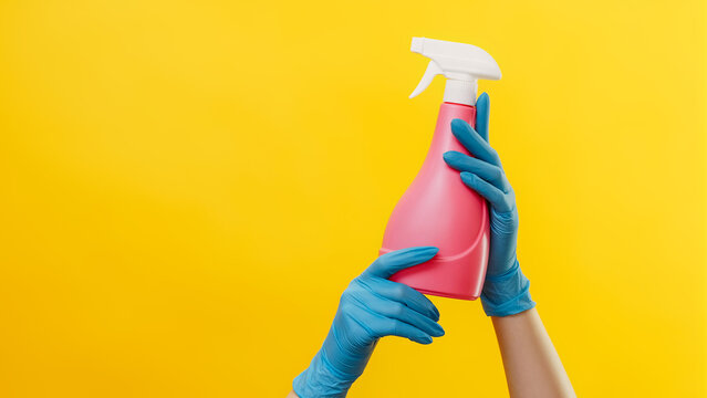 Detergent advertising. Cleaning quality. Housekeeper hands in blue rubber gloves with pink spray bottle isolated on yellow background empty space.