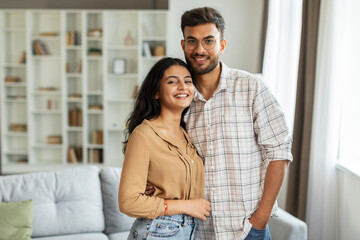 Portrait of young romantic indian couple embracing and smiling, posing in living room interior, enjoying time together, free space