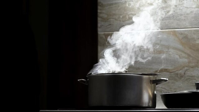 Steam is coming from a pot on the electric stove on black background. Boiling water or soup. Slow motion shot.