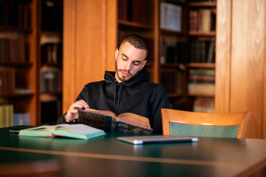 Male student sitting at desk in the university library and reading book for learning