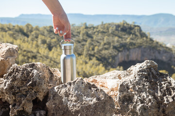 Hand taking an aluminum thermal bottle to hydrate on a hiking trail