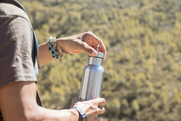 Hand taking an aluminum thermal bottle to hydrate on a hiking trail