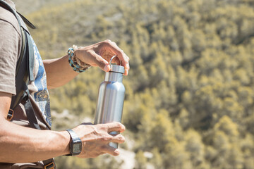 Hand taking an aluminum thermal bottle to hydrate on a hiking trail