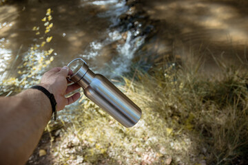 Hand taking an aluminum thermal bottle to hydrate on a hiking trail