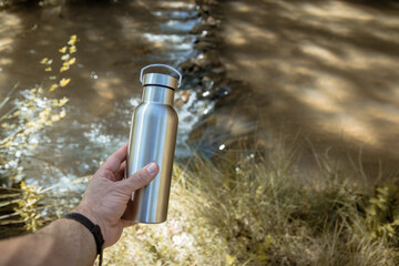 Hand taking an aluminum thermal bottle to hydrate on a hiking trail